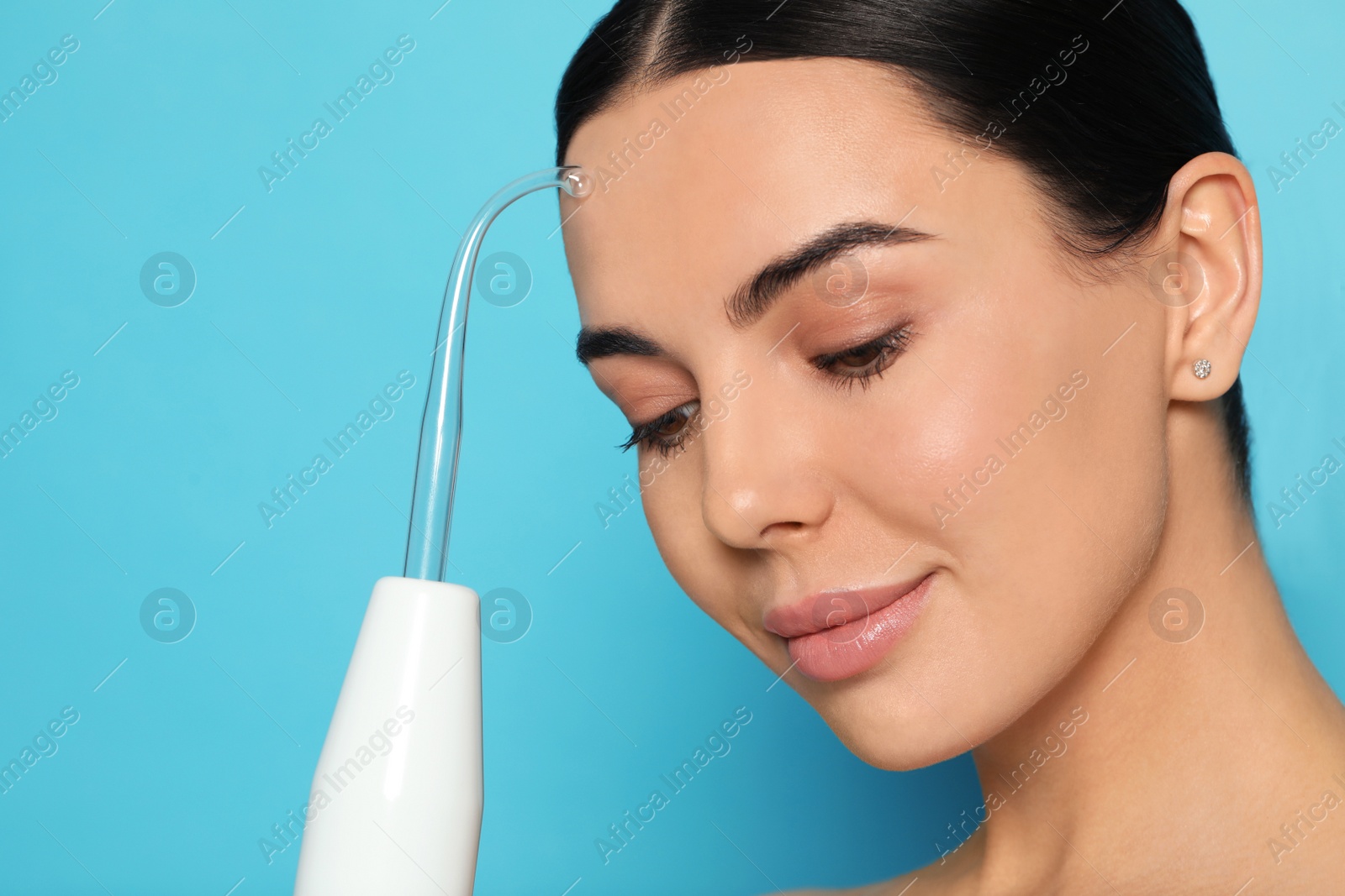 Photo of Woman using high frequency darsonval device on light blue background. Space for text