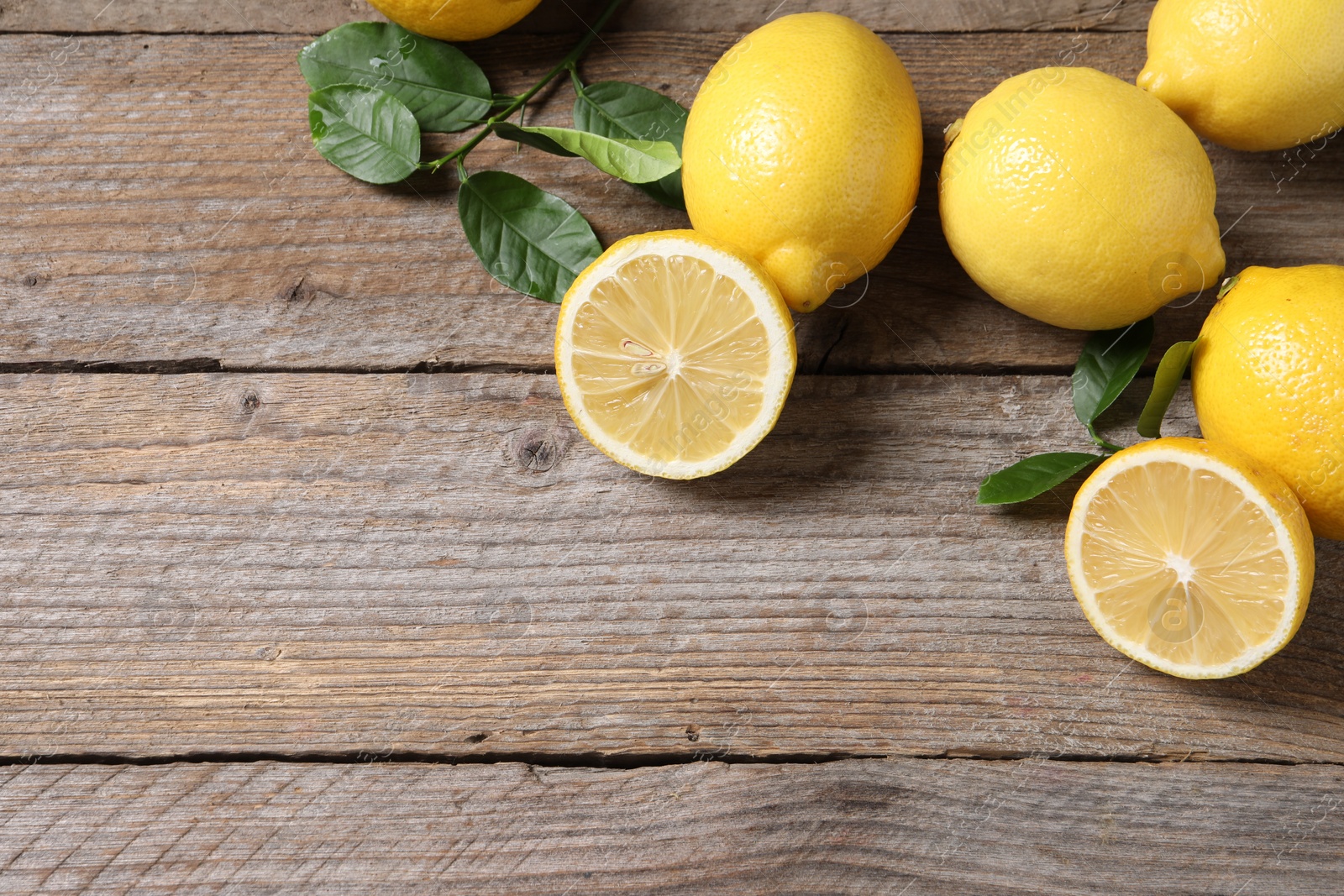 Photo of Fresh lemons and green leaves on wooden table, flat lay. Space for text