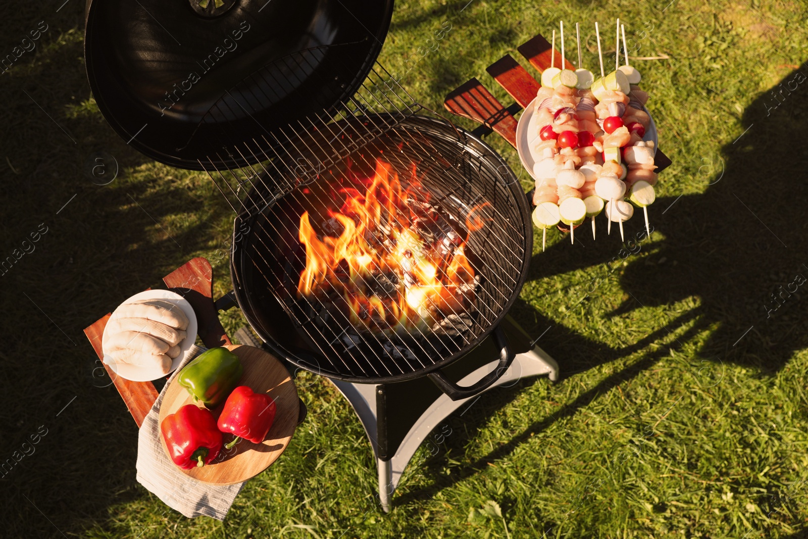 Photo of Skewers with meat and vegetables near barbecue grill outdoors, top view