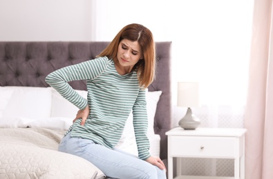 Photo of Young woman suffering from back pain at home