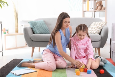 Photo of Child psychologist and little girl playing with cubes in office