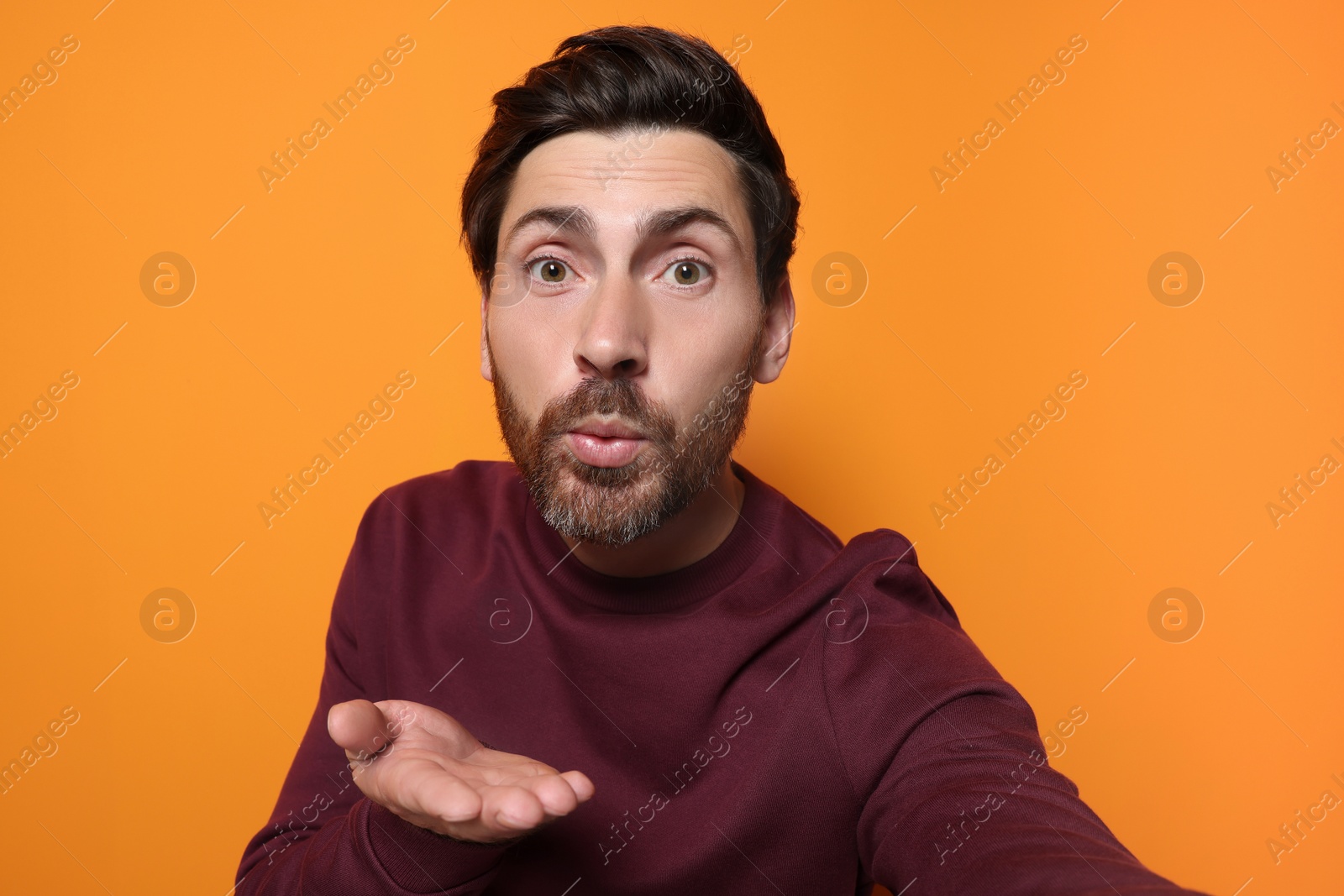 Photo of Handsome man blowing kiss while taking selfie on orange background