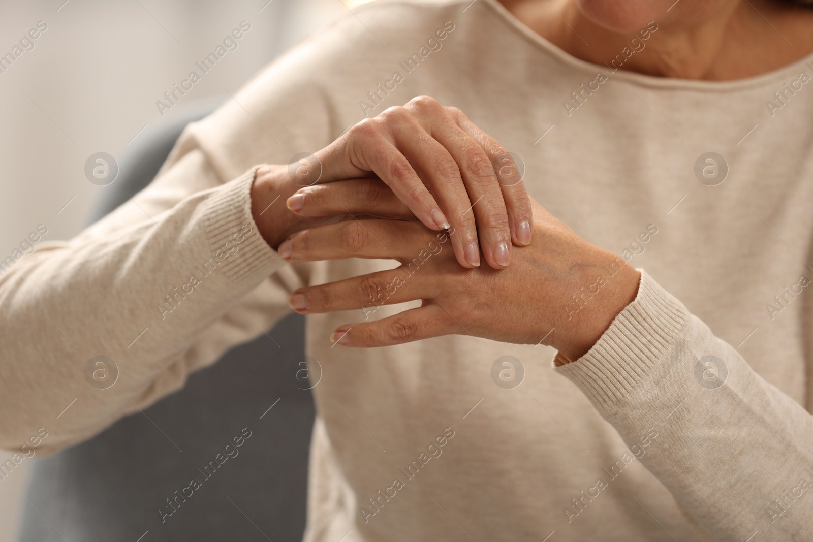 Photo of Mature woman suffering from pain in hand on blurred background, closeup. Rheumatism symptom