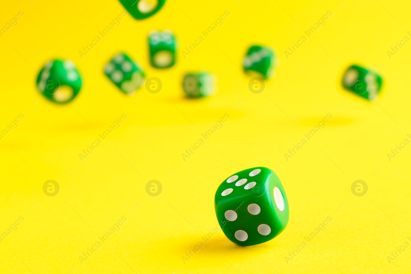 Photo of Many green game dices falling on yellow background