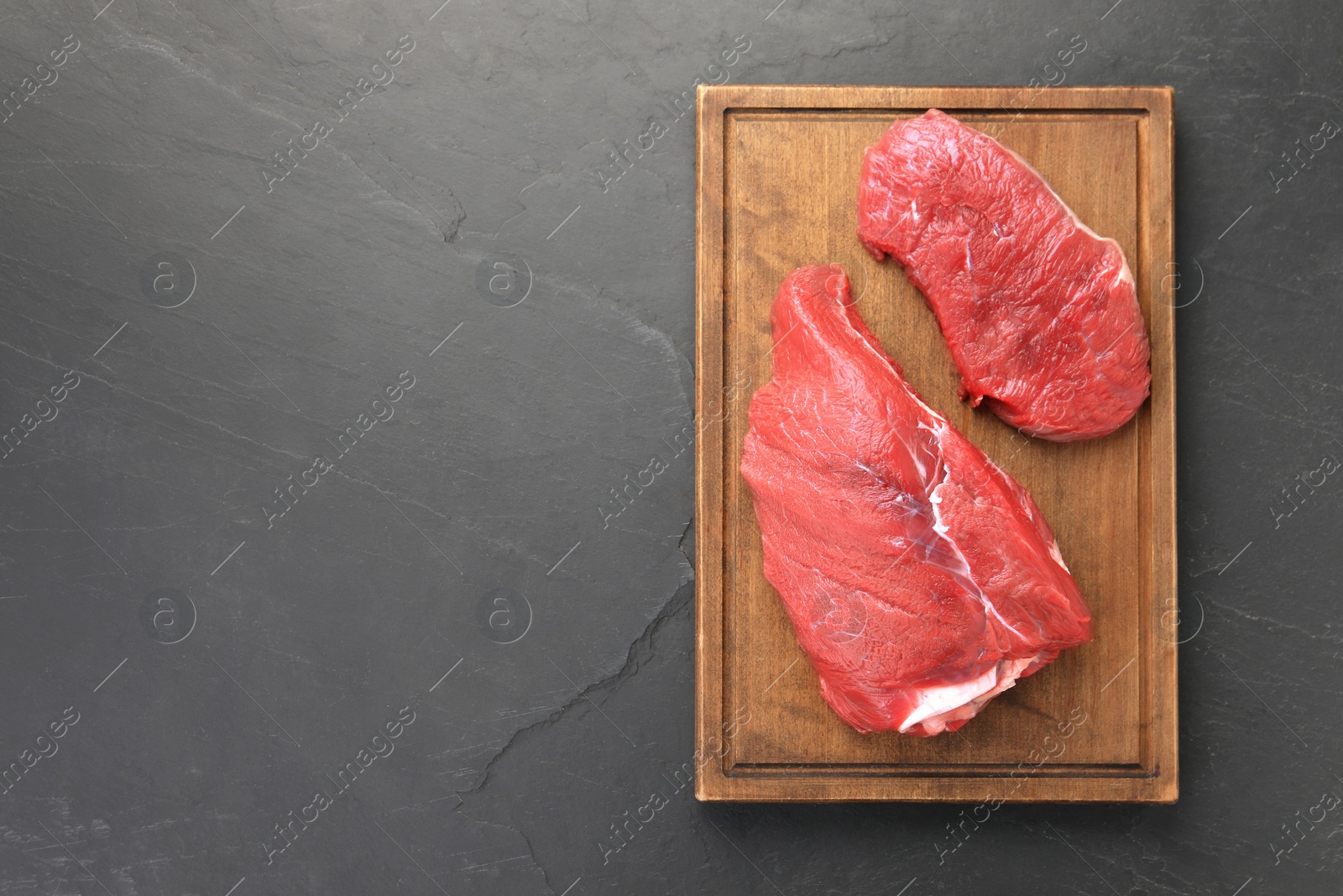 Photo of Pieces of raw beef meat on black table, top view. Space for text