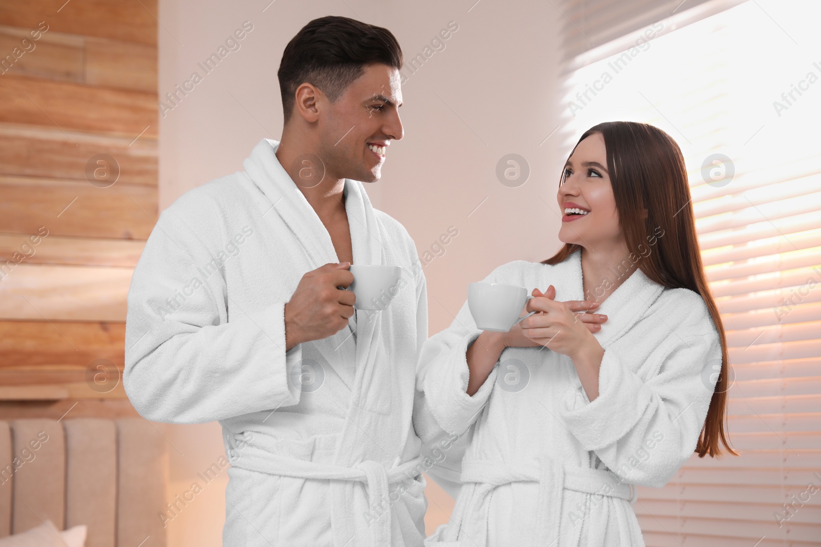 Photo of Happy couple in bathrobes with coffee in bedroom