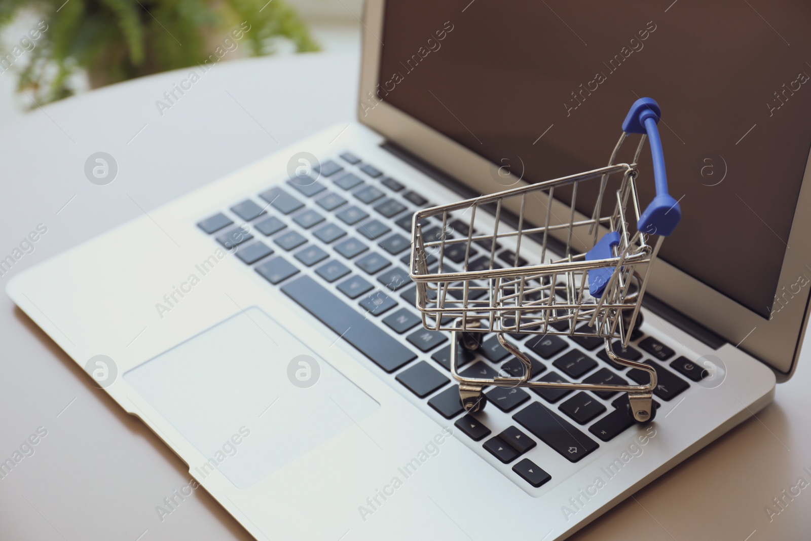 Photo of Internet shopping. Laptop with small cart on table indoors, closeup