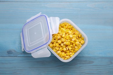 Photo of Plastic container with corn kernels and lid on light blue wooden table, top view
