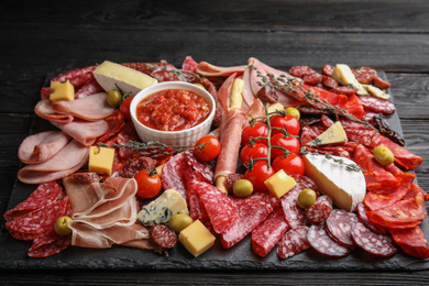 Photo of Tasty ham with other delicacies served on black wooden table