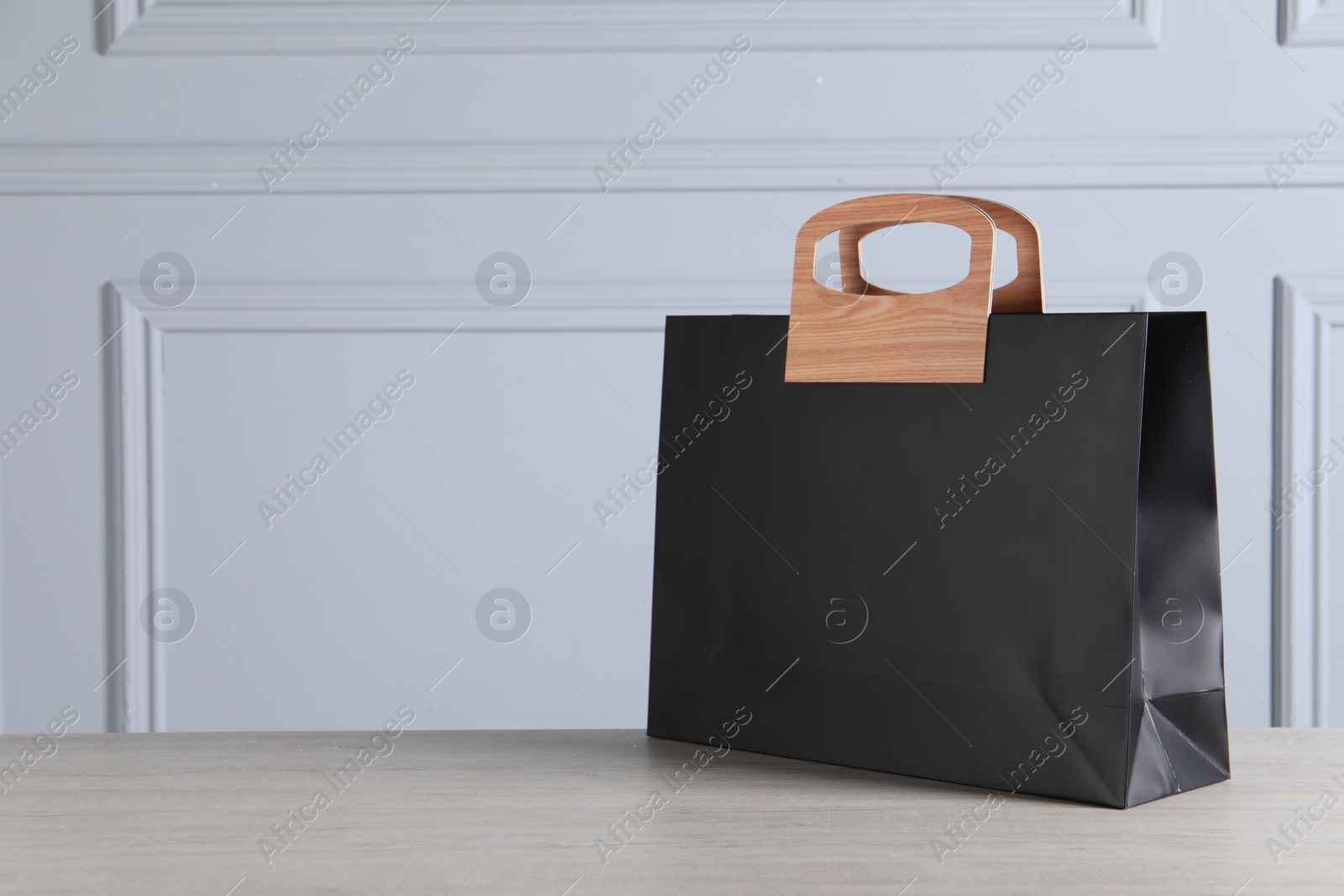 Photo of Black paper bag on wooden table against light grey wall, space for text