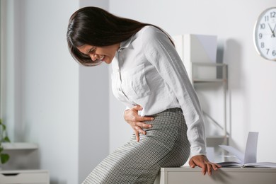 Photo of Young woman suffering from menstrual pain in office