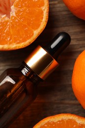 Bottle of tangerine essential oil and fresh fruits on wooden table, top view