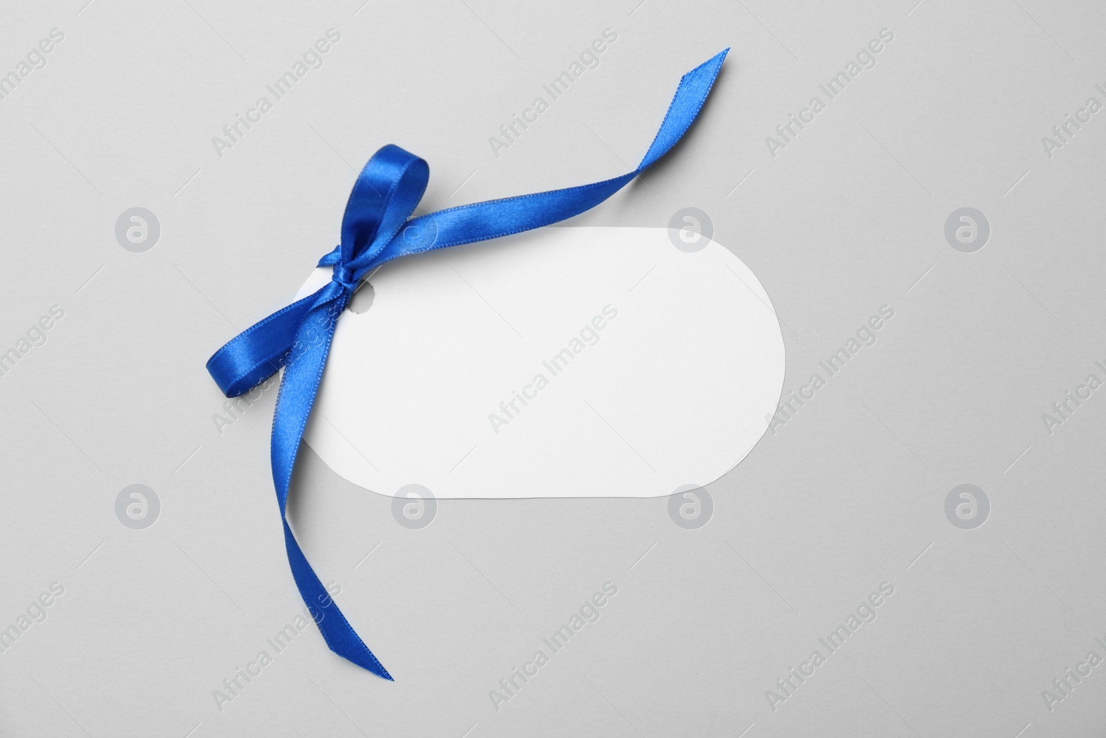 Photo of Blank gift tag with satin ribbon on light background, top view