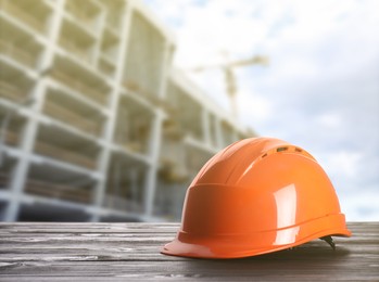 Image of Hard hat on wooden surface at construction site with unfinished building. Space for text 