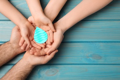 Image of Family holding paper water drop on blue wooden background, top view. Space for text