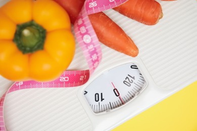 Photo of Scales, vegetables and measuring tape on yellow background, top view