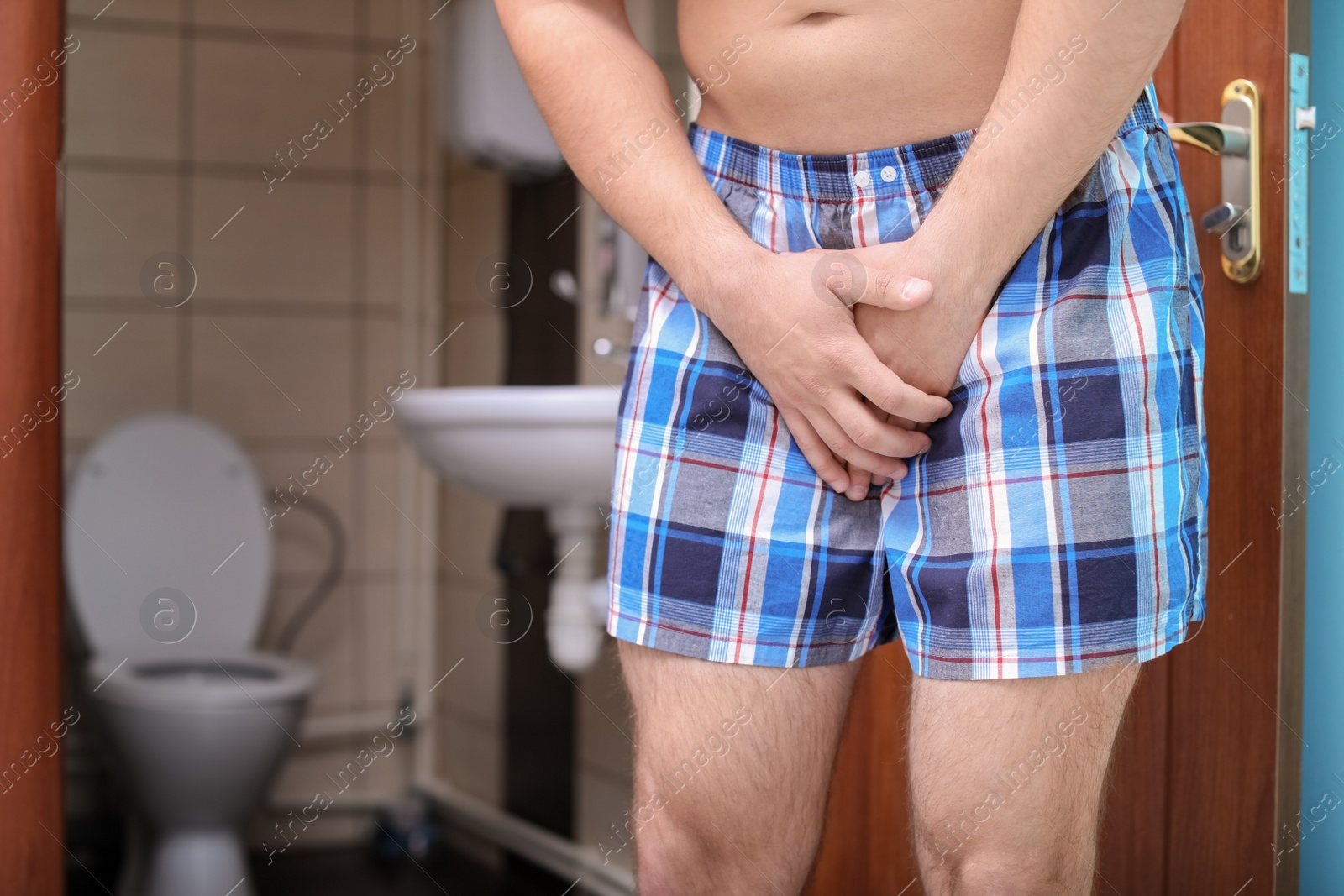 Photo of Young man with urological problems suffering from pain near toilet