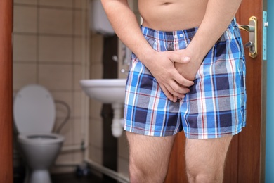 Photo of Young man with urological problems suffering from pain near toilet