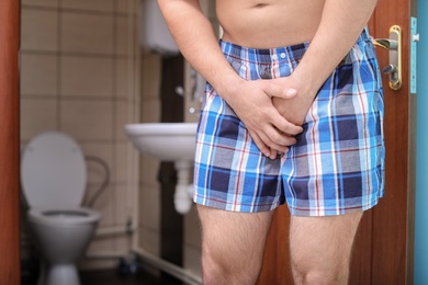 Young man with urological problems suffering from pain near toilet