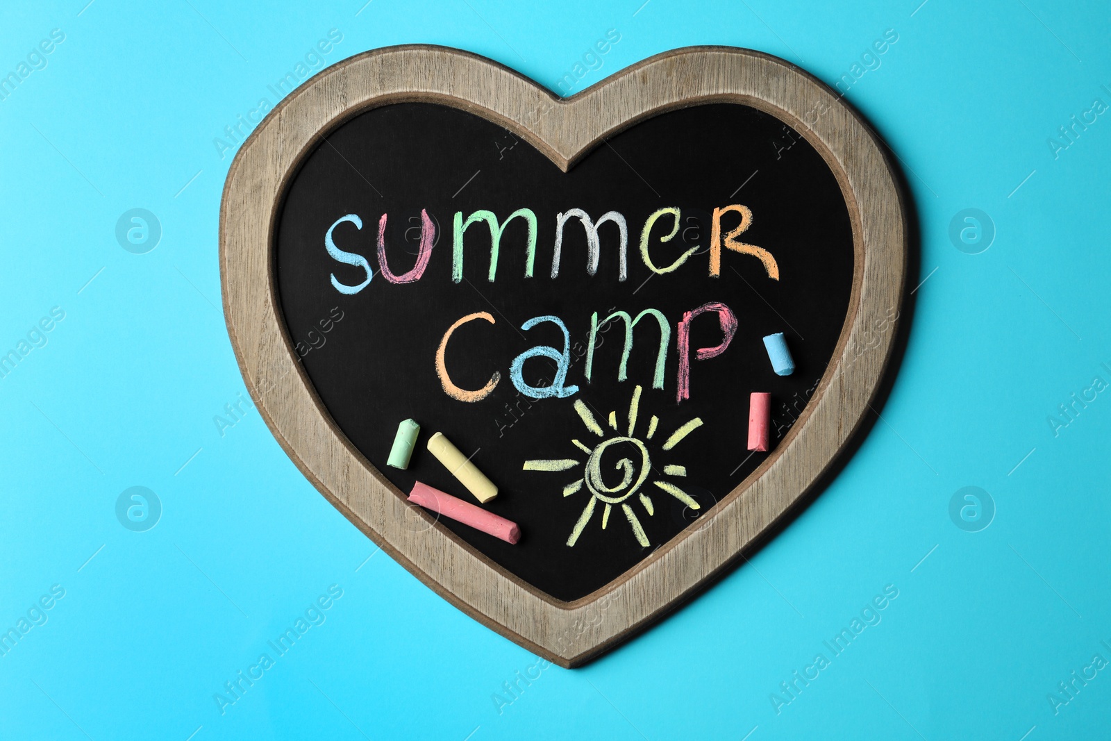 Photo of Heart shaped blackboard with text SUMMER CAMP, drawing and chalk sticks on color background, top view