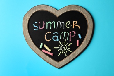 Heart shaped blackboard with text SUMMER CAMP, drawing and chalk sticks on color background, top view