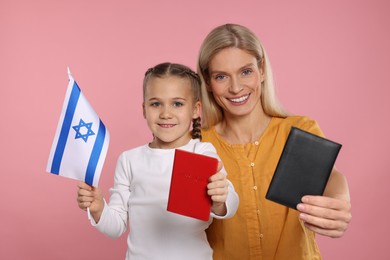 Photo of Immigration. Happy woman with her daughter holding passports and flag of Israel on pink background