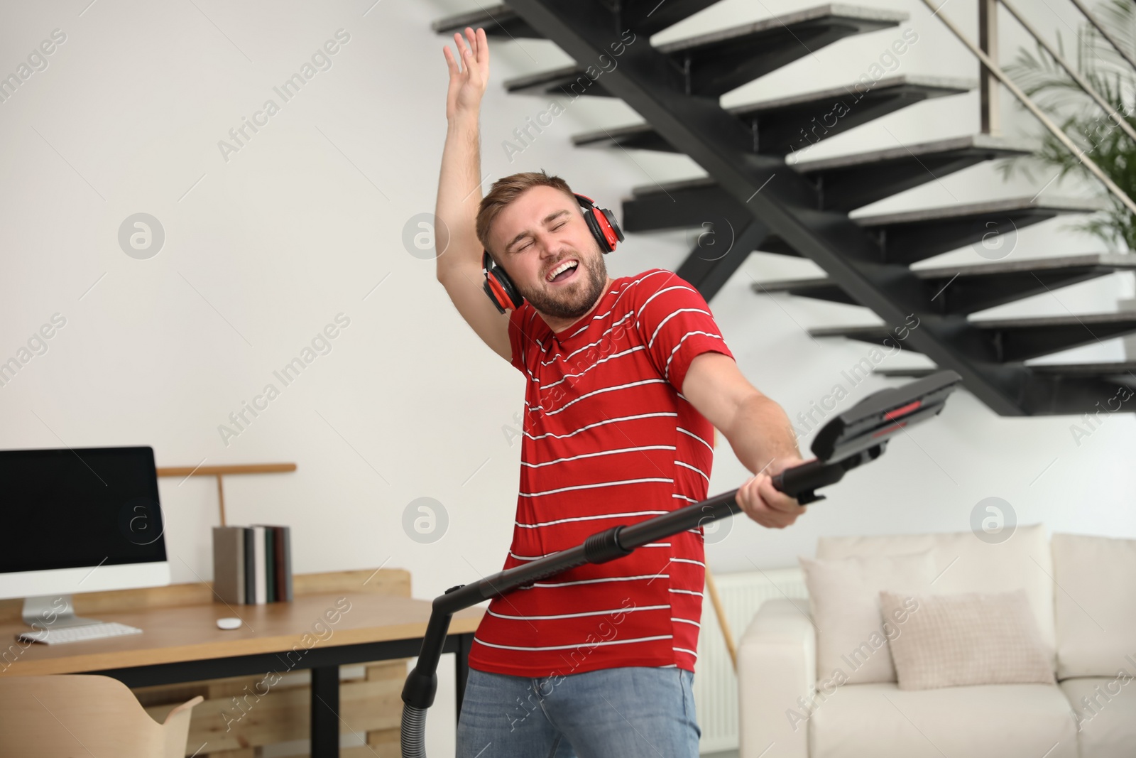 Photo of Young man having fun while vacuuming in living room