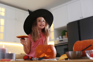 Photo of Little girl with pumpkin jack o'lantern at table in kitchen. Halloween celebration