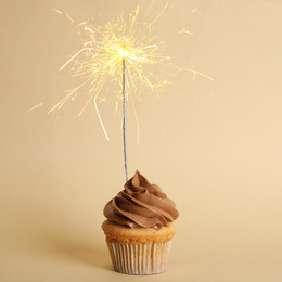 Birthday cupcake with sparkler on beige background