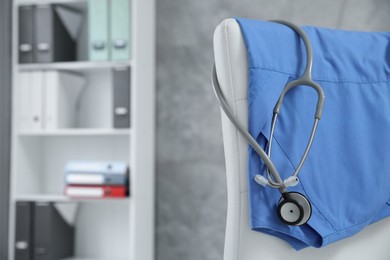 Photo of Blue medical uniform and stethoscope hanging on chair in clinic, closeup. Space for text