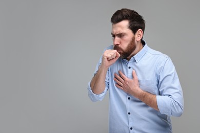 Sick man coughing on light grey background, space for text. Cold symptoms