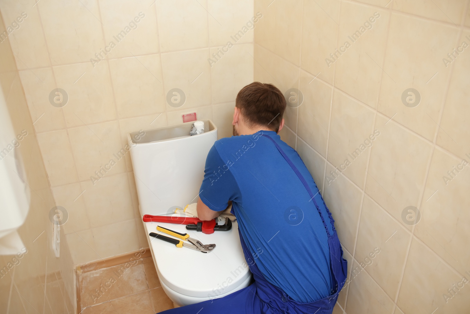 Photo of Professional plumber in uniform fixing toilet tank indoors