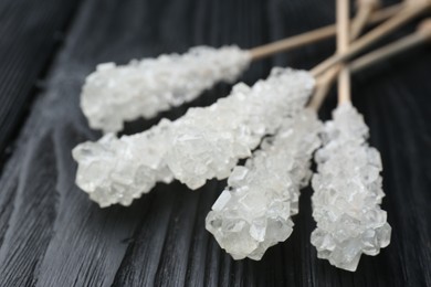 Sticks with sugar crystals on black wooden table, closeup. Tasty rock candies