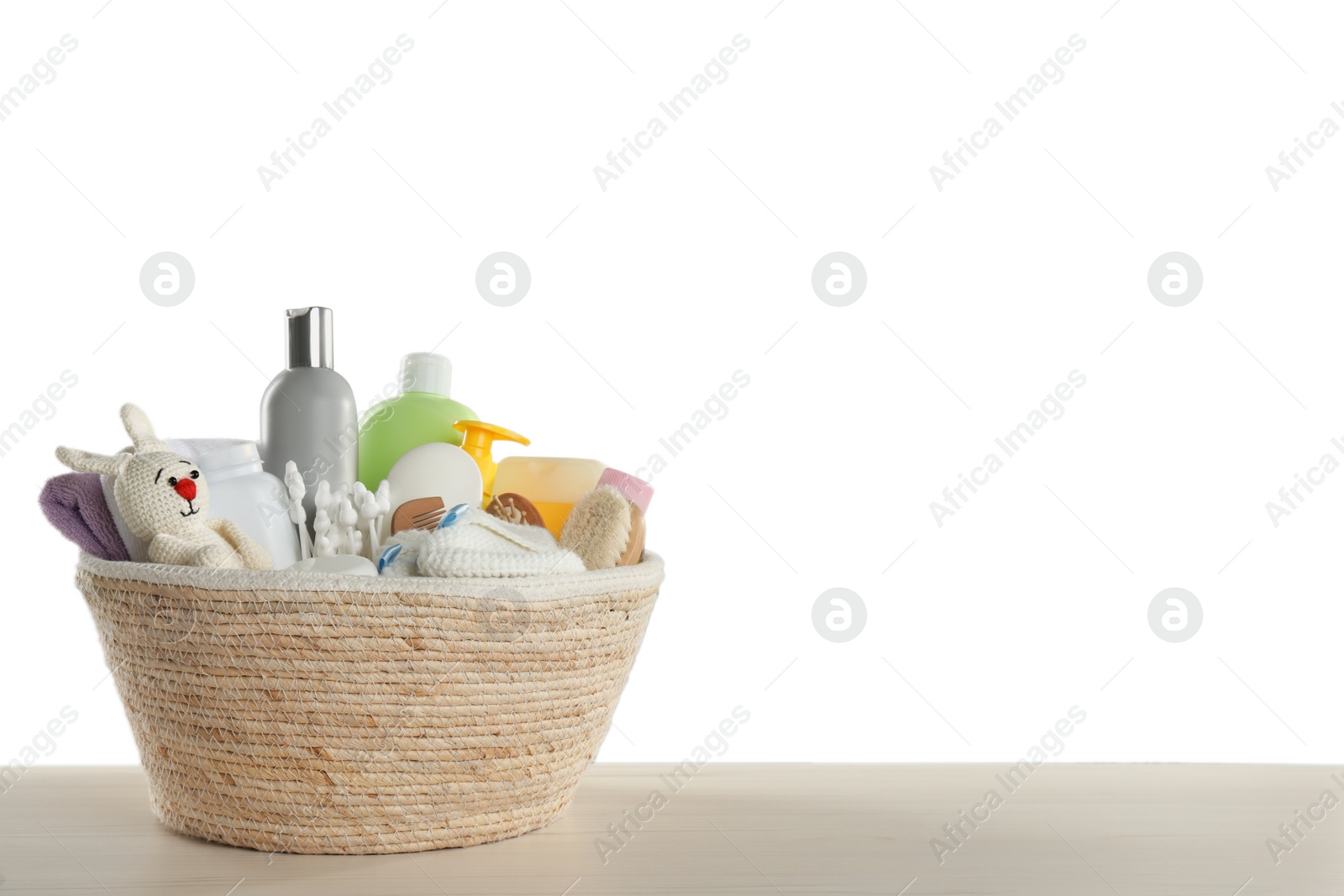 Photo of Wicker basket full of different baby cosmetic products, bathing accessories and toy on wooden table against white background