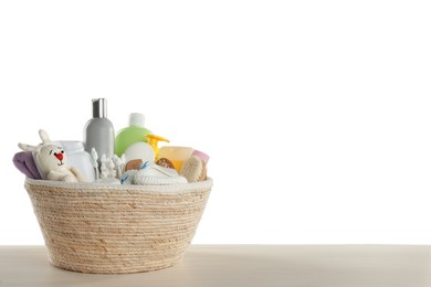 Photo of Wicker basket full of different baby cosmetic products, bathing accessories and toy on wooden table against white background