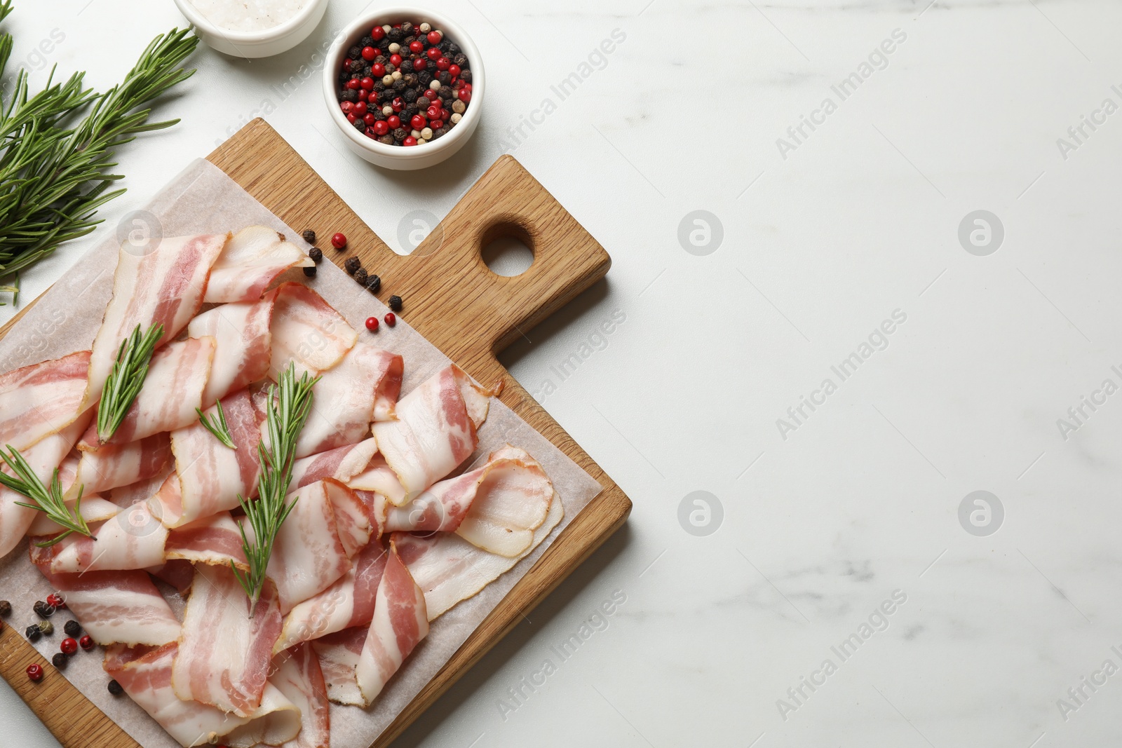 Photo of Slices of raw bacon and spices on white marble table, flat lay. Space for text