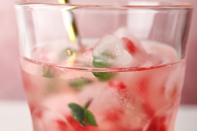 Glass of tasty cocktail with pomegranate ice cubes on color background, closeup