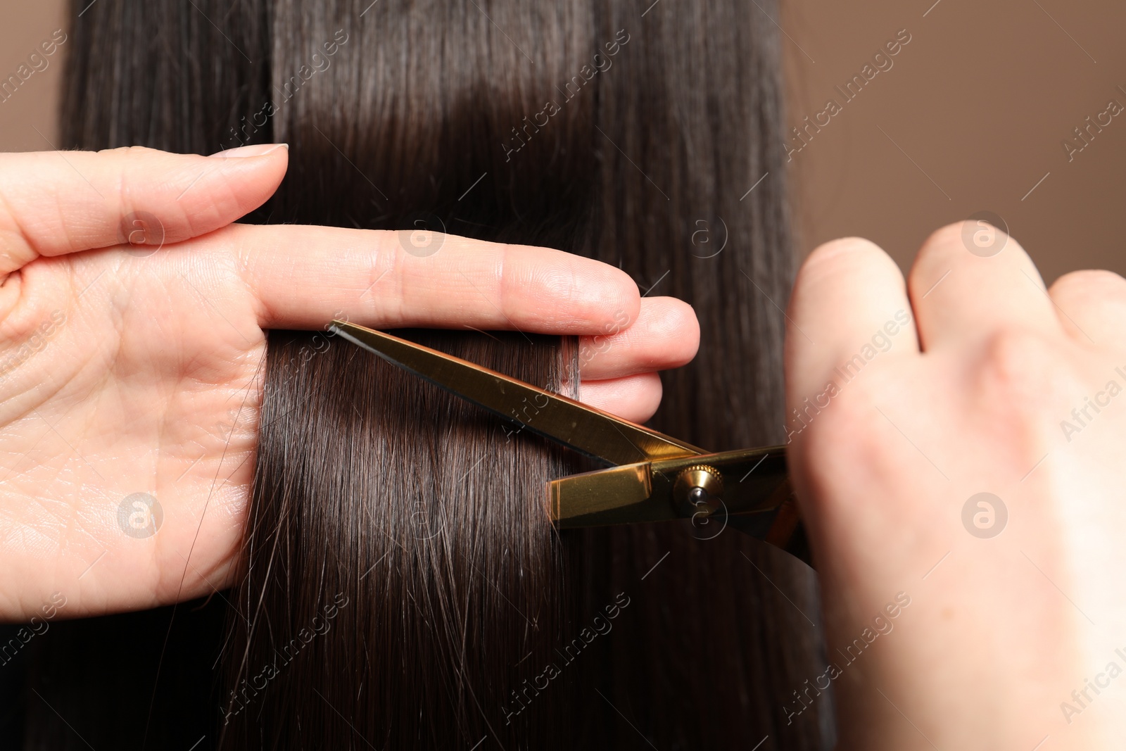 Photo of Hairdresser cutting client's hair with scissors on light brown background, closeup