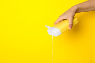 Photo of Woman pouring cosmetic product from bottle on yellow background, closeup. Space for text