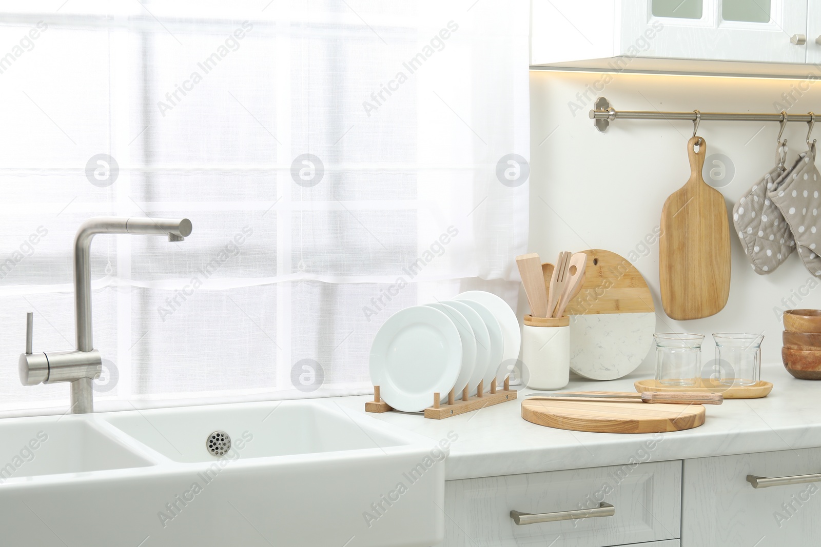Photo of Wooden cutting boards, other cooking utensils and dishware on white countertop near sink in kitchen