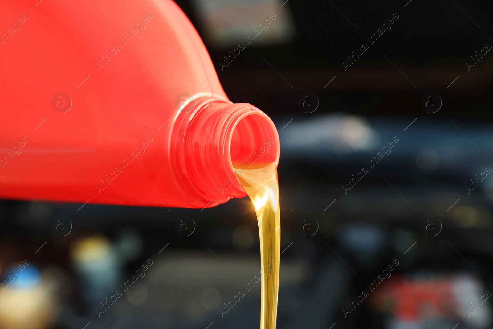 Photo of Pouring motor oil from red container on blurred background, closeup. Space for text