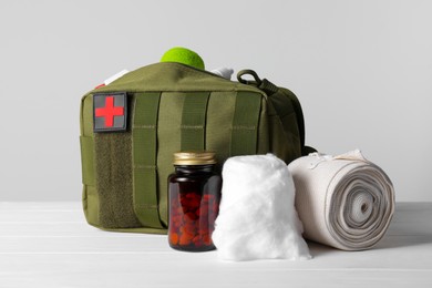 Photo of Military first aid kit, medical cotton, pills and elastic bandage on white wooden table