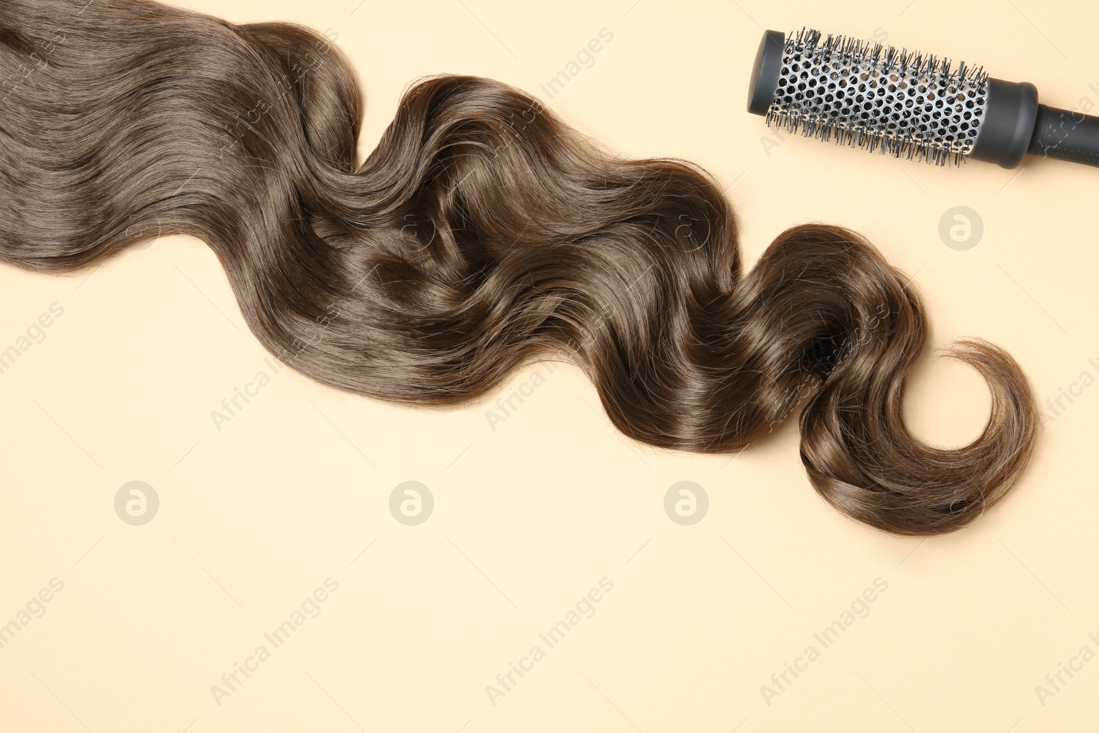 Photo of Lock of brown wavy hair and brush on color background, flat lay. Space for text