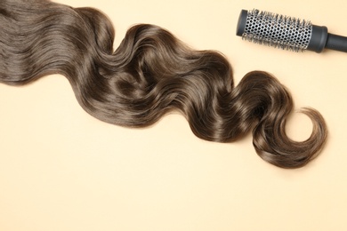 Lock of brown wavy hair and brush on color background, flat lay. Space for text