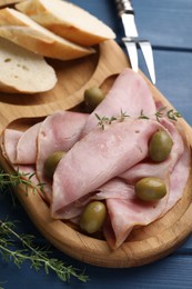 Photo of Slices of delicious ham with olives and baguette served on blue wooden table, closeup