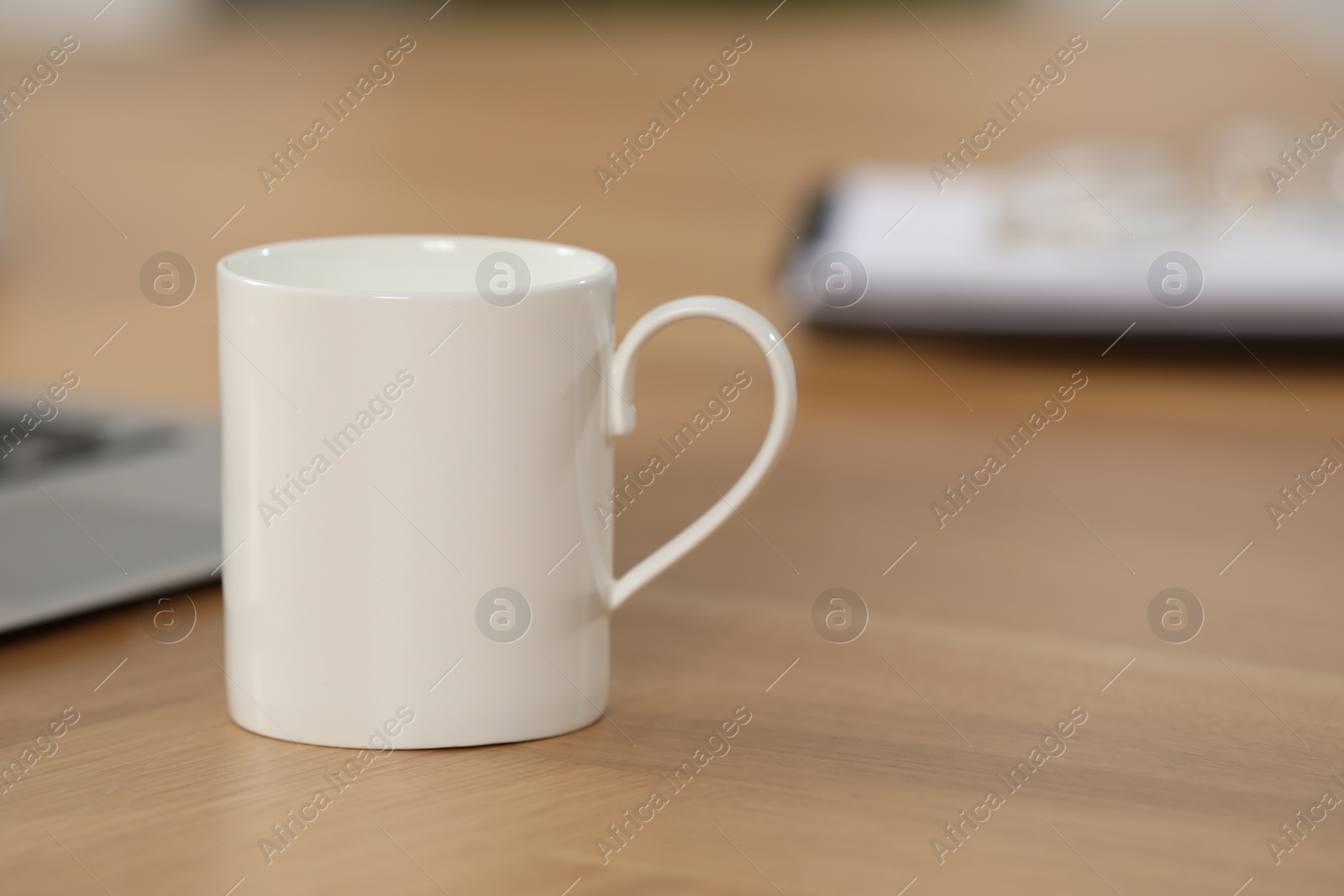 Photo of White ceramic mug on wooden table at workplace. Space for text