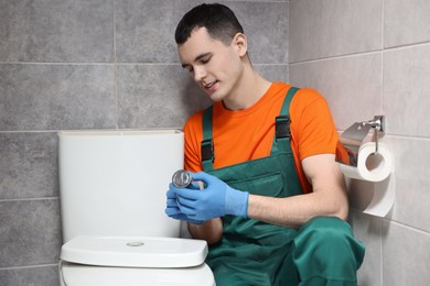 Photo of Young plumber repairing toilet bowl in water closet