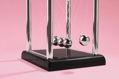 Photo of Newton's cradle on pink background, closeup. Physics law of energy conservation