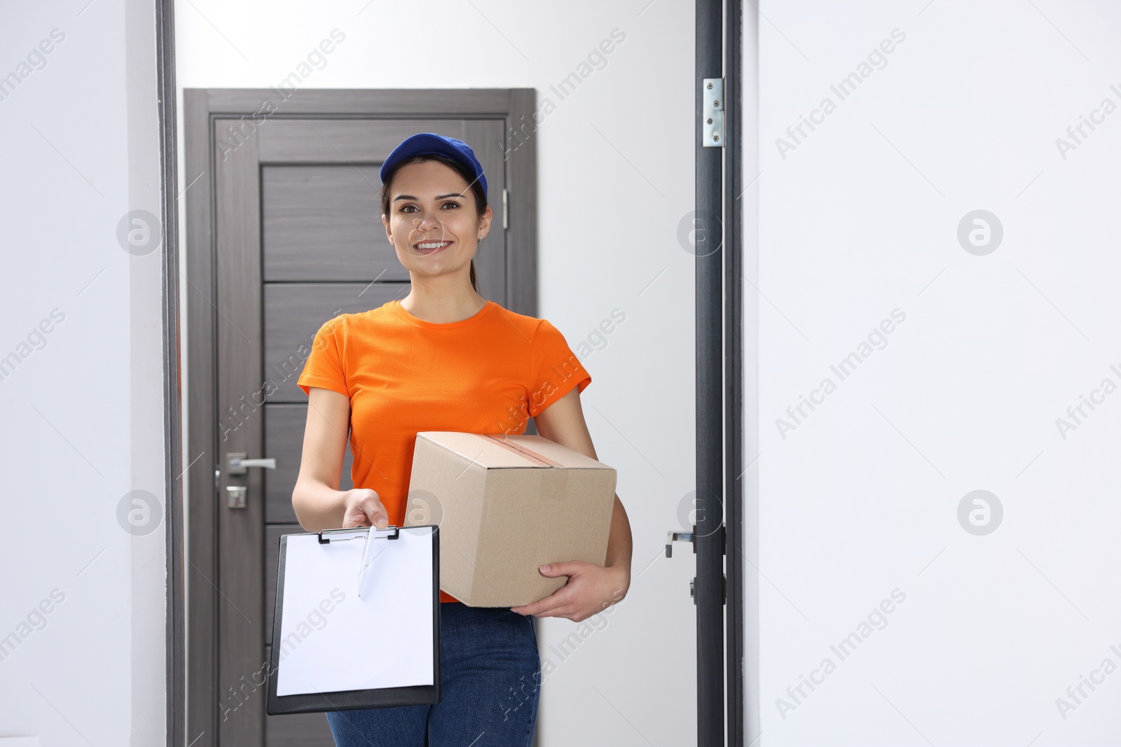 Photo of Smiling courier holding parcel and clipboard in hallway, space for text