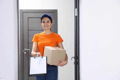 Smiling courier holding parcel and clipboard in hallway, space for text